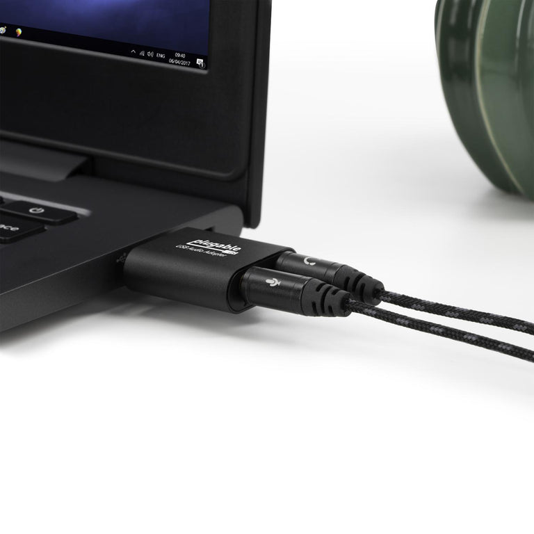 A close up image of the USB-AUDIO adapter plugged into a USB port on a computer, and headphone and microphone jacks plugged in.