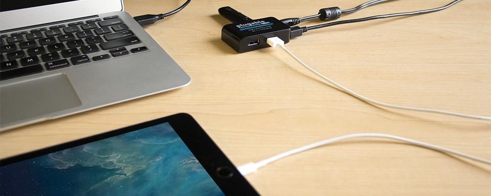 Highlight of the usb2-hub4bc on a desk connected to a laptop, charging an iPad, and a USB thumb drive connected.